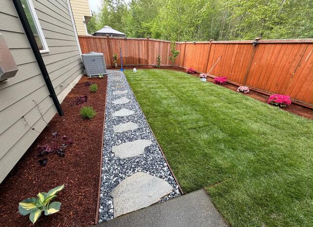 New sod side yard with stepping stones, red mulch, and a cedar fence