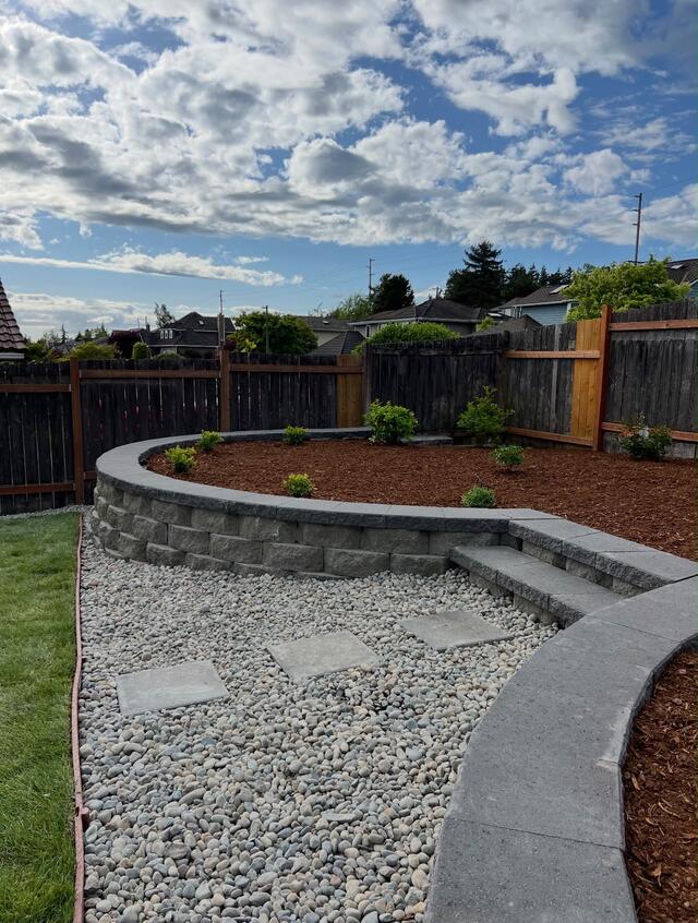 Curved block retaining wall with gravel beds in a backyard