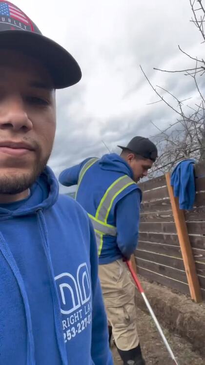 A Bright Lawn crew member in a branded hoodie on a job site, with a second crew member raking behind him