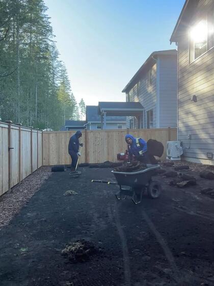 Two crew members spreading topsoil from a wheelbarrow across a bare back yard