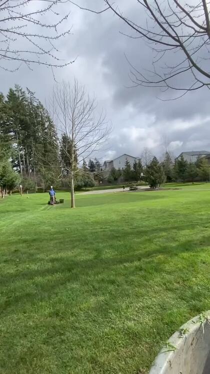 A wide open green lawn with a crew member mowing in the distance